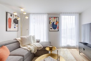 A modern living room with a sectional sofa, a flat-screen TV, abstract art, and a floor lamp. - Old Port 2BR | Pool Gym Parking (Montreal)