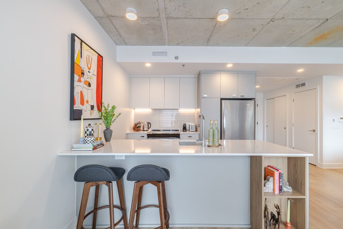 A modern kitchen with white cabinetry, a stainless steel refrigerator, and a central island with bar stools.
