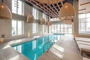 Ein überdachter Pool mit großen Fenstern, klaren Glaswänden und hängenden Pendelleuchten.