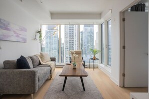 Ein modernes Wohnzimmer mit einer Couch, einem Couchtisch und Blick auf hohe Gebäude durch große Fenster.