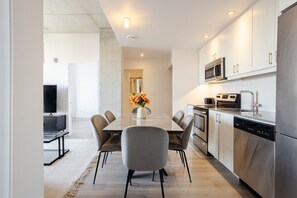 A modern kitchen with stainless steel appliances, a dining area with a table and chairs, and a TV in the background. - The Old Port Skyline Retreat – A Montreal Getaway (Montreal)