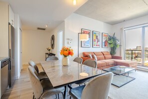 A modern living room with a glass coffee table, a sofa, a dining table, and a kitchen area with a refrigerator. - The Old Port Skyline Retreat – A Montreal Getaway (Montreal)