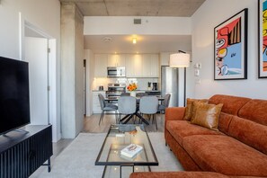 A modern living room with a sofa, a coffee table, and a TV. There is a kitchen in the background with a dining area. - The Old Port Skyline Retreat – A Montreal Getaway (Montreal)