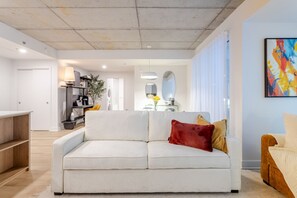 A modern living room with a white sofa, a wooden coffee table, and a kitchen area in the background. - Old Montreal Haven – Bright, Spacious & Walkable (Montreal)