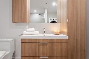A bathroom with a wooden vanity, a white sink, a mirror, and a lit candle on the counter. - Old Montreal Haven – Bright, Spacious & Walkable (Montreal)