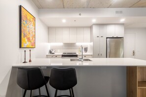 Eine moderne Küche mit weißen Schränken, einem Edelstahlkühlschrank und einer Bar mit zwei schwarzen Stühlen.