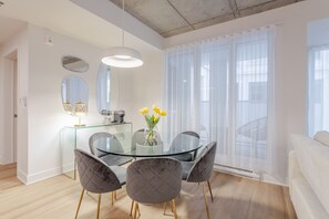 A modern dining area with a glass table, four cushioned chairs, a vase with yellow flowers, and a large window with sheer curtains. - Old Montreal Haven – Bright, Spacious & Walkable (Montreal)