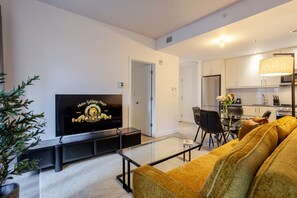 A modern living room with a flat-screen TV, a sofa, a coffee table, and a dining area with chairs. - The Old Port Hideaway (Montreal)