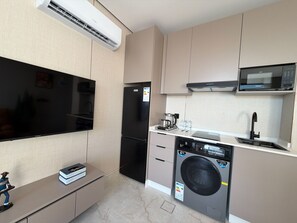 Een compacte keuken met een ingebouwde magnetron, een koelkast, een wasmachine en een flatscreen-televisie.