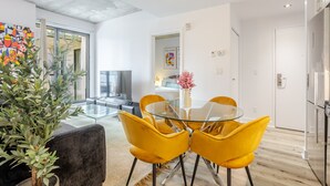 Una sala de estar moderna con una mesa de vidrio, sillas amarillas, una planta en maceta y un ventanal grande.