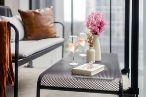 Un balcon avec un canapé, une table avec un livre et des verres, et un vase rempli de fleurs.