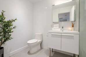 Un baño moderno con inodoro, lavamanos con espejo y una planta en maceta.