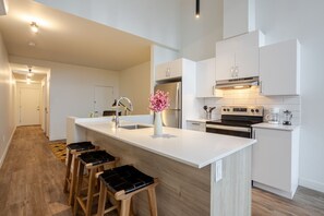 Une cuisine moderne dotée d’un îlot central, d’appareils électroménagers en acier inoxydable et de tabourets en bois.