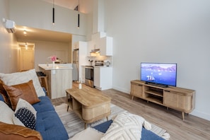 A modern living room with a sofa, coffee table, TV, and kitchen area. - MTL Trendy Hideaway in Rosemont (Montreal)