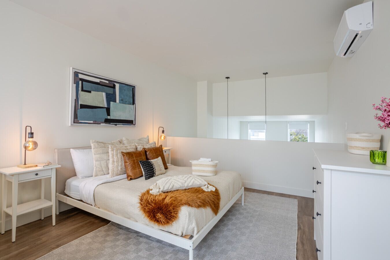 Un dormitorio moderno con cama, mesitas de noche, un espejo y una ventana.