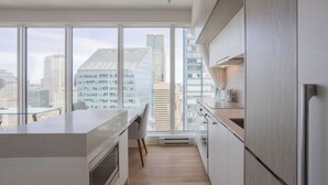 Una cocina moderna con un ventanal amplio, muebles blancos y vistas a edificios de la ciudad.