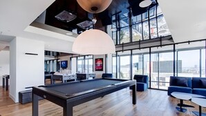 Una mesa de billar moderna en un espacio interior con techo alto y grandes ventanales.
