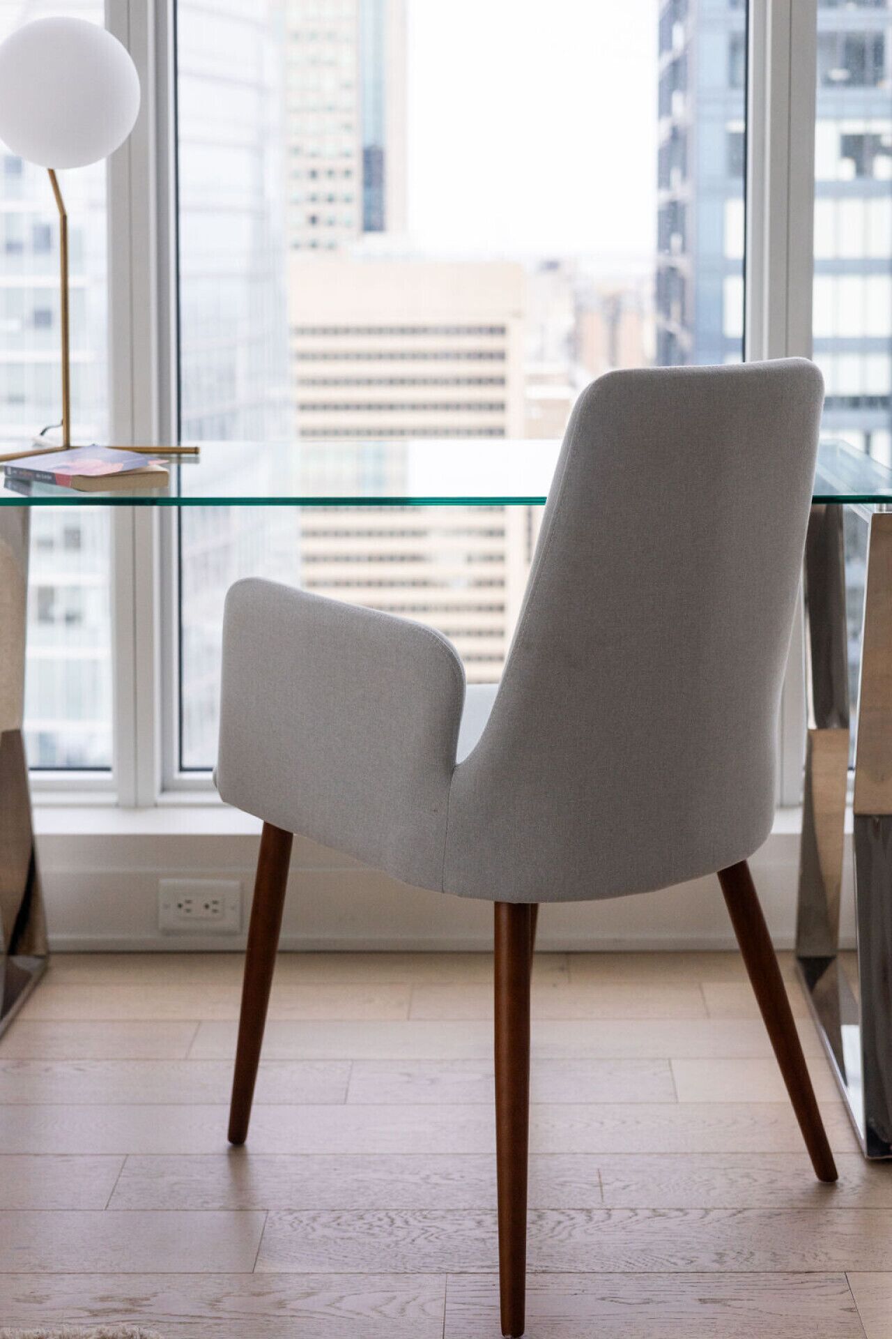 A chair with a high back and wooden legs, positioned in front of a window with a view of buildings.
