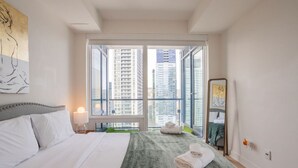 Habitación de hotel con cama, ventana grande, espejo y vista de edificios altos.