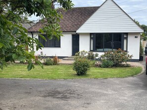 A single-story house with a sloped roof, a front porch, and a small front yard with various plants. - Family Beach Home in Highcliffe, Dorset / New Forest with 10 Min walk to beaches (Christchurch)
