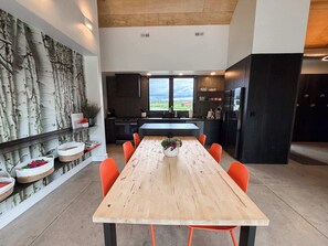 Eine moderne Küche mit einer großen Kochinsel, einem Essbereich mit Holztisch und orangefarbenen Stühlen und Blick auf die Landschaft durch die Fenster.