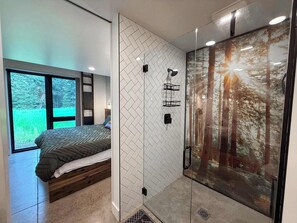 Ein modernes Schlafzimmer mit Bett, einer Duschkabine aus Glas und einem großen Fenster.