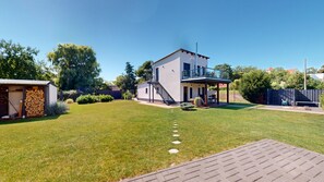 Een modern huis met twee verdiepingen, een overdekt terras, een kleine schuur en een verzorgd gazon.