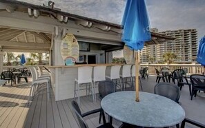 Ein Außenbereich mit Tischen, Stühlen, einer Bar und Blick auf ein Gebäude im Hintergrund.
