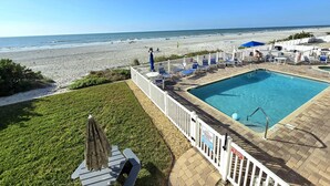 Ein Poolbereich mit Blick auf den Strand, eine umzäunte Terrasse und Liegestühle.