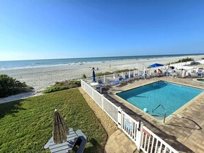 Ein Poolbereich mit Blick auf den Strand, eine umzäunte Terrasse und Liegestühle.