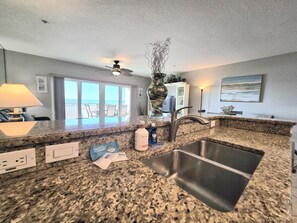A kitchen with granite countertops, a stainless steel sink, a ceiling fan, and a view of the ocean through large sliding doors. - Double the Views, Double the Fun at Ocean Side Building with direct Gulf Views (Indian Rocks Beach)