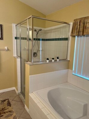 Une salle de bain avec une douche à parois de verre, une baignoire et une fenêtre avec des rideaux.