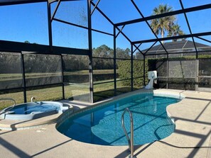 Une piscine avec un jacuzzi, entourée d’une structure en verre, et donnant sur un terrain de golf.