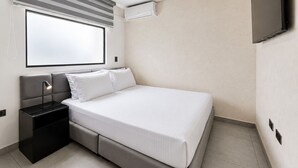 A modern hotel room with a bed, bedside table, lamp, air conditioning unit, and a TV mounted on the wall. - Apartaestudio Luxury (Sabaneta)