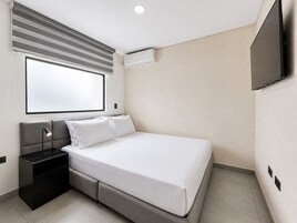 Una habitación de hotel moderna con cama, mesita de noche, lámpara, equipo de aire acondicionado y un televisor montado en la pared.