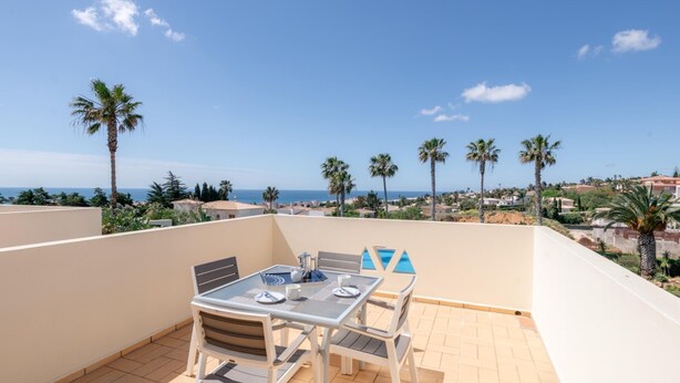 Eine Terrasse mit Tisch und Stühlen, ein Pool und Meerblick mit Palmen.
