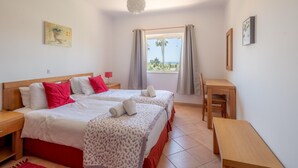 Ein Doppelbett mit roter und weißer Bettwäsche, ein Nachttisch, ein Schreibtisch, ein Stuhl, ein Fenster mit Vorhängen und eine Hängelampe.