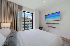 Une chambre d’hôtel avec un grand lit, un téléviseur fixé au mur, une fenêtre avec des rideaux et une vue sur les bâtiments environnants.
