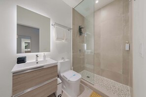 Une salle de bain moderne avec un lavabo blanc, un miroir et des toilettes, une douche en verre et un carrelage décoratif au sol.