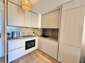 Una cocina moderna con armarios blancos, horno empotrado, lavabo y lámpara colgante.