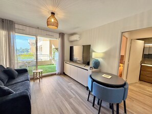 Quarto de hotel moderno com sofá, uma mesa de jantar com cadeiras, televisão, abajur e vista para o exterior.