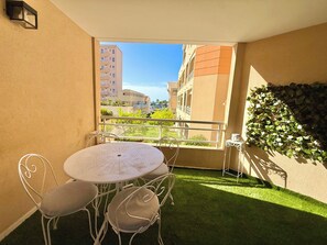A balcony with a round table and chairs, a small white table, and a wall-mounted planter with green foliage.