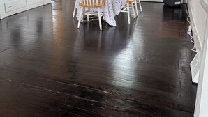Uma sala de jantar com uma mesa posta para quatro pessoas, cercada por cadeiras brancas, um ventilador de teto e uma janela com cortinas.