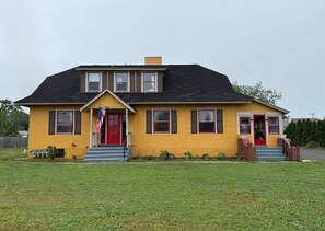 Ein zweistöckiges Haus mit roter Tür, einer Veranda und einer Flagge.