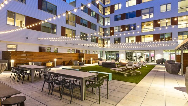 Een moderne hotelbinnenplaats met buiten zitplaatsen, een gazon en lichtjes.