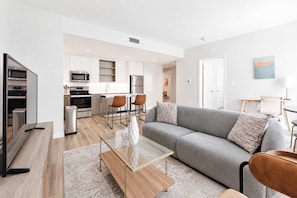 A modern living room with a grey sofa, a glass coffee table, and a TV. - Modern Apartment | Gym + Courtyard (Cambridge, MA)