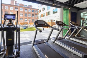 A gym with treadmills and a stationary bike, large windows, and a view of buildings outside. - Modern Apartment | Gym + Courtyard (Cambridge, MA)