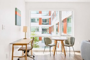 A modern room with a desk, two chairs, a lamp, and a large window with a view of a building. - Modern Apartment | Gym + Courtyard (Cambridge, MA)