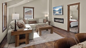 A living room with a sofa, two coffee tables, a fireplace, and a painting on the wall. - Strawberry Moon in Whitefish with Hot Tub (Whitefish)