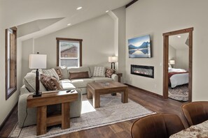 A living room with a sofa, two coffee tables, a fireplace, and a painting on the wall. - Strawberry Moon in Whitefish with Hot Tub (Whitefish)